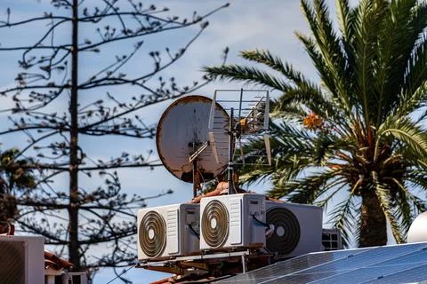 A satellite dish is mounted on a rooftop with two air conditioners Stock Photos