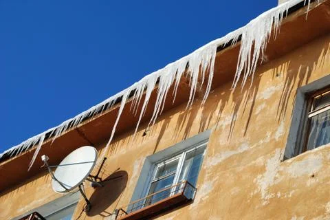 Satellite receiver dish on the wall with  icicles and blue sky behind Stock Photos