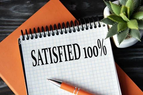 SATISFIED 100%- words in white notebook on dark wooden background with cact.. Stock Photos