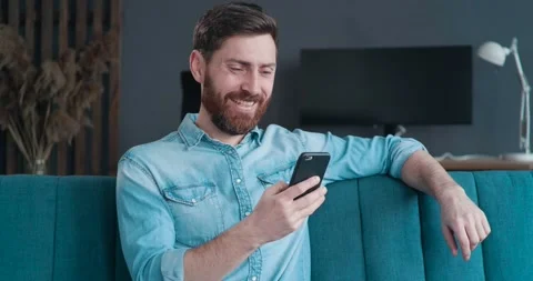 Satisfied Bearded Man is relaxing on the Couch at Home, chatting with Friends. Stock Footage 136592259