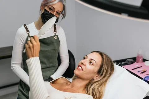 Satisfied client checking microblading results in mirror at beauty salon Stock Photos