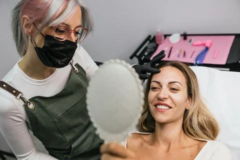 Satisfied client checking new eyebrows in mirror after microblading session Stock Photos