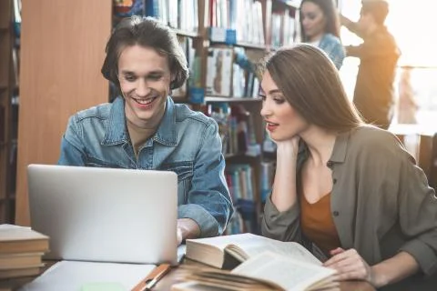 Satisfied comrades using laptop in library Stock Photos