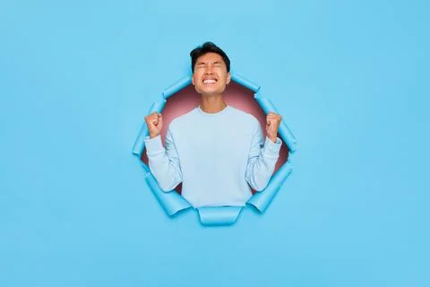 Satisfied guy in white sweatshirt throws up his arms happily, posing in the Stock Photos