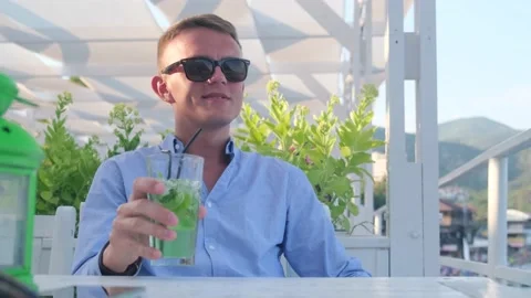Satisfied happy man drinking refreshing cocktail in cafe with sea view Video stock 158299294