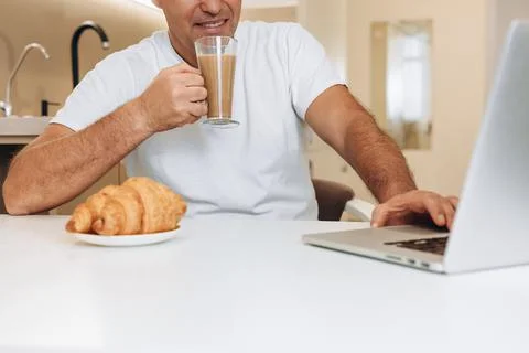 Satisfied man drinks latte or coffee with milk and uses his modern laptop Foto stock