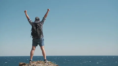 Satisfied man standing on mountain top and raising his arms to the sky Stock Footage 137345213