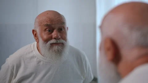 Satisfied old Caucasian man caressing long white beard smiling looking in mirror Stock Footage 231368682