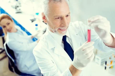 Satisfied researcher smiling while looking at test tube with liquid Stock Photos
