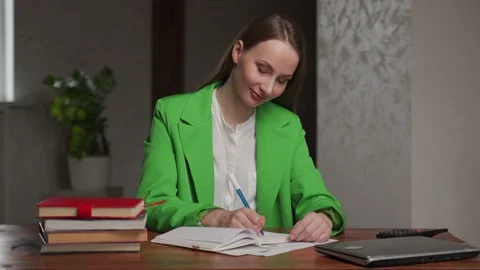 Satisfied teacher writes notes in exercise book at table Stock-Footage 194526688