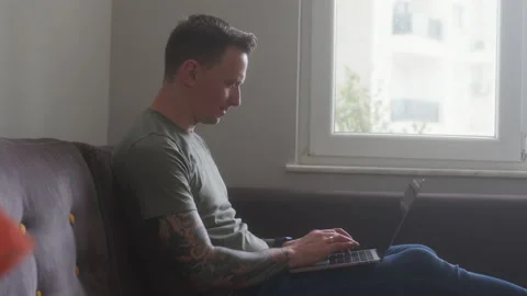 Satisfied young guy freelancer sit on sofa with laptop in his hands and work Stock Footage 232639965