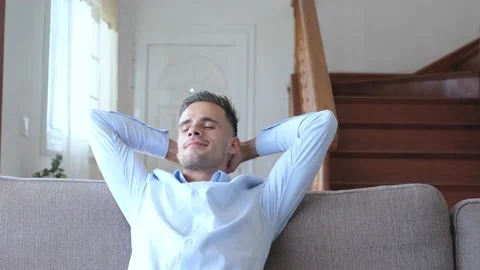 Satisfied young man relaxing while sitting on couch with hands behind back at ho Stock Footage 171898862