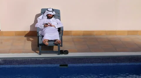 Saudi arabian man using his phone at swimming pool Stock Footage 12176055