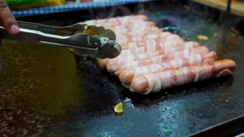 Sausage with bacon frying on a griddle Stock Footage 295401097