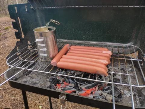 Sausages and can of beans are getting heated on the grill. Stock Photos