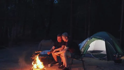 Sausages are fried over a fire. Adventurers Campfire Evening, surrounded by the Stock Footage 318070917