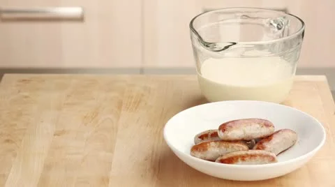 Sausages being placed in a hot baking dish and batter being poured over them Stock Footage 24671764