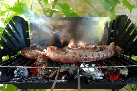 Sausages cooking on a basic barbeque on a summers evening Stock Photos
