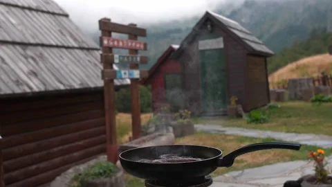 Sausages frying in a pan while camping in the mountains village Stockbeeldmateriaal 220058975