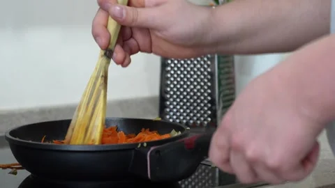 Sautéing vegetables in a pan, hand stirs the carrots with a wooden spatula Stock Footage 301290763