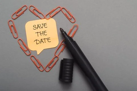 Save the date is written on a yellow post it is surrounded by red paper clips Stock Photos