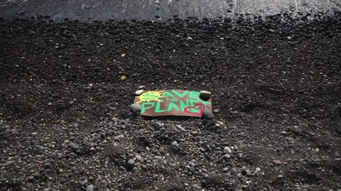 The "Save the Planet" poster lies on the black volcanic Stock Footage 167016692