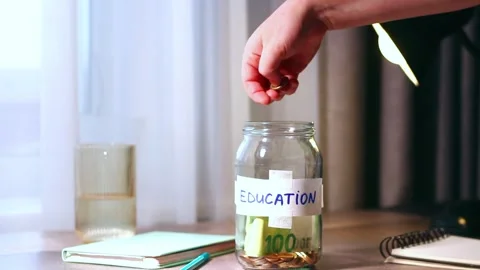 Saving for education fund using money jar. Young person carefully placing money 스톡 동영상 329687733