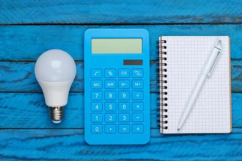Saving electricity. Led light bulb and calculator, notebook on blue wooden ba Stockfoto's