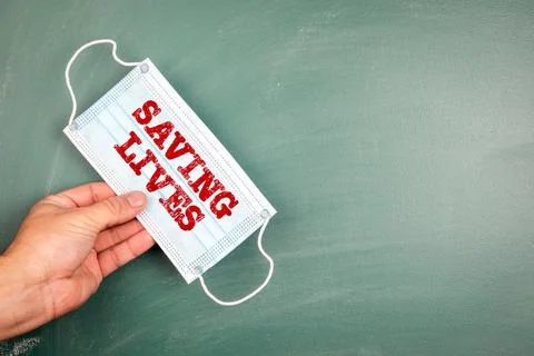 SAVING LIVES. Face mask in a man 's hand. Green chalk board Stock Photos