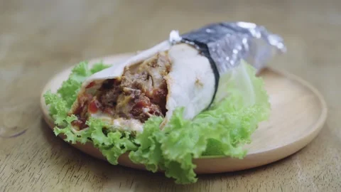 Savory meat wrap or kebab partially wrapped in foil, served on a fresh gree.. Stock Footage 336492242