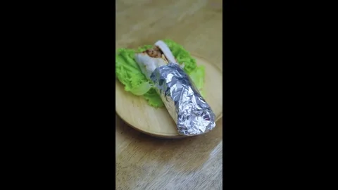 Savory meat wrap or kebab partially wrapped in foil, served on a fresh gree.. Stock Footage 336838074