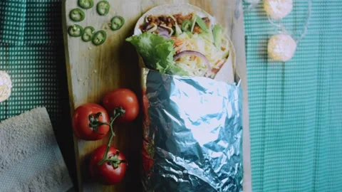 Savory serving view: serving a foil-wrapped burrito on a rustic table Stock Footage 342168205
