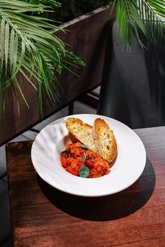 Savory tomato dish served with bread in a cozy dining setting Stock Photos