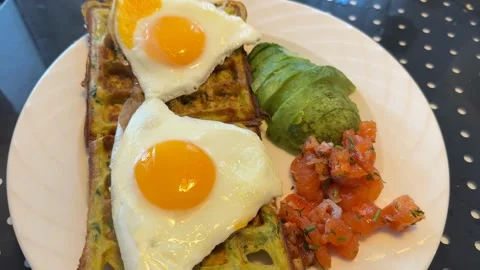 Savory waffle breakfast with fried eggs, avocado, and salsa on a white plat.. Vídeos de archivo 331031068