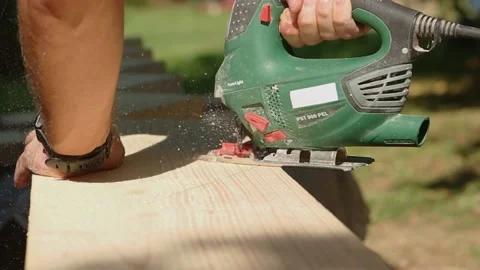 Saw-Man's hands with clock is sawing wooden block with electric jigsaw Stock Footage 231795223