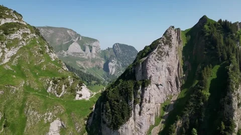 Saxer Lucke Diagonal Flight Over Alpine Cliff and Green Valley Stock Footage 323331215