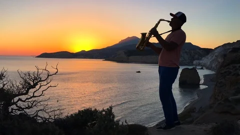 The saxophonist plays in the rays of the sunset on a cliff overlooking the sea Stock Footage 86560934