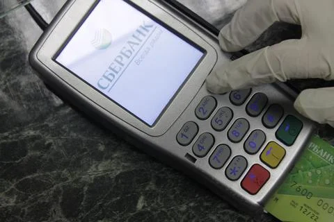 Sberbank client wearing medical gloves enters a password into the PINpad. Sbe Stock Photos