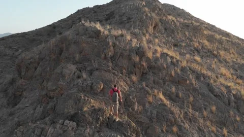 Scaling steep rocks off the path, a man in shorts and a red shirt with trek.. Stock Footage 286054297