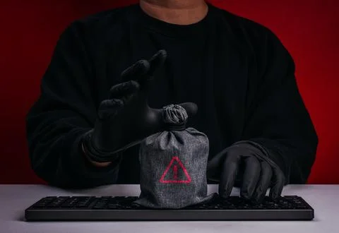 Scammer or hacker sits behind keyboard with warning-marked money bag. Digit.. Stock Photos