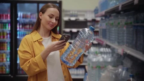 Scanning a bottle of water in a store while checking information on a mobile 스톡 동영상 305414863