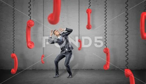 A scared businessman on concrete background hides from many red retro phone Stock Photos