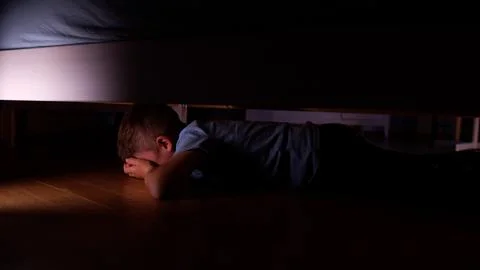 Scared child hiding under the bed at night Stock Photos
