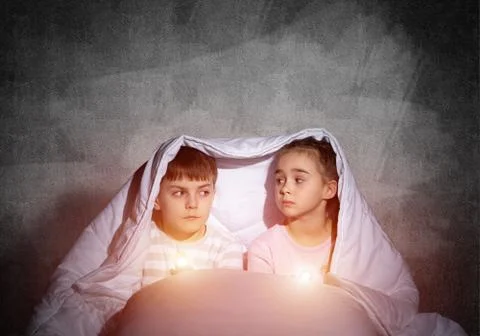 Scared children with flashlights in bed Stock Photos