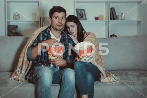 The scared couple eating popcorn and watch a horror movie on the sofa Stock Photos
