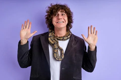 Scared curly guy stand with spread arms frightened by python Foto stock