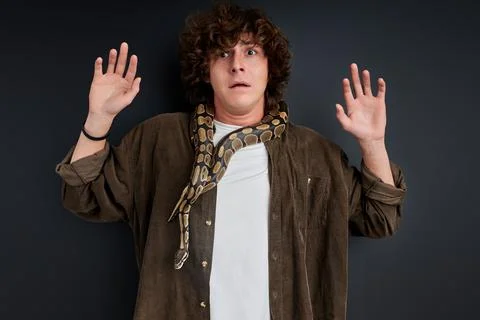 Scared curly guy stand with spread arms frightened by python Stock Photos