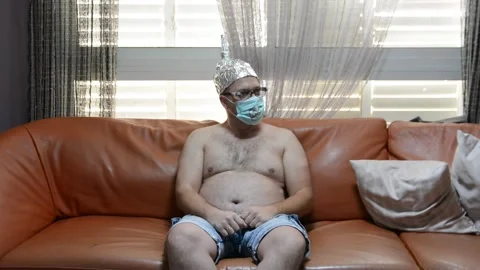 Scared freak man on a sofa in a foil hat and glasses drink beer. freak man with  Stock Footage 130879226