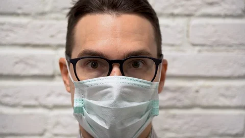 Scared man in black glasses, protective medical mask covers mouth in horror  Stock Footage 127783037