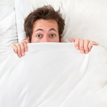 Scared man hiding in bed Stock Photos